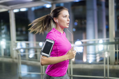 Young woman in pink sportshirt running in city at night