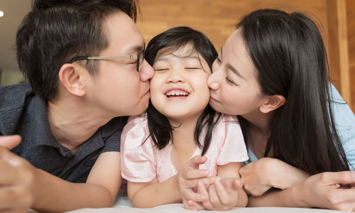 Close-up of father and mother kissing daughter lying on bed