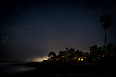 Silhouette trees by sea against sky at night