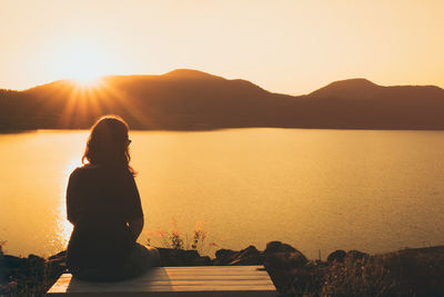 Rear view of woman looking at lake against clear sky