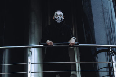 Low angle view of young man wearing mask standing by railing