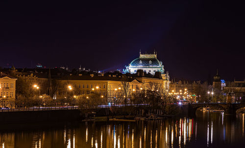 Illuminated buildings by river against sky at night