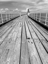 Wooden footbridge on pier by sea against sky