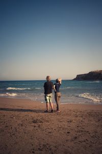 Friends on shore at beach against clear sky