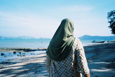 Rear view of woman standing at beach against sky