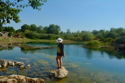 Side view of woman standing by lake against sky