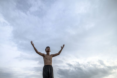 Low angle view of shirtless boy standing against cloudy sky