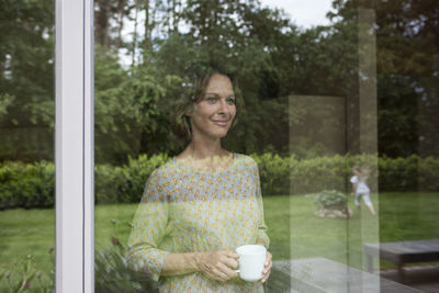 Smiling woman holding cup looking out of window