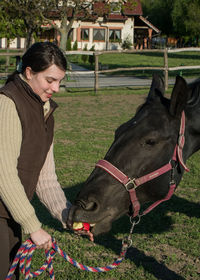 Young woman feeding horse in animal pen