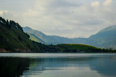 Scenic view of lake by mountains against sky during foggy weather