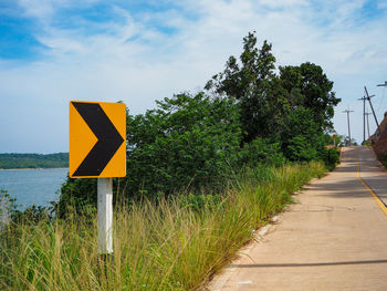 Information sign on road by trees against sky