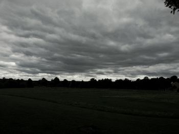 Silhouette trees on landscape against cloudy sky