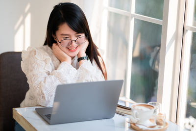 Young woman using phone while sitting on table