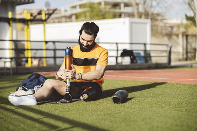 Disabled athlete adjusting prosthetic leg sitting on grass