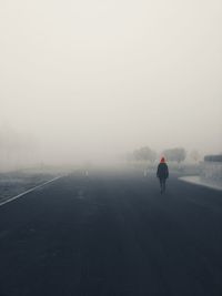 Rear view of man walking on snow covered landscape in foggy weather