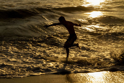 Silhouette man standing on beach by sea during sunset