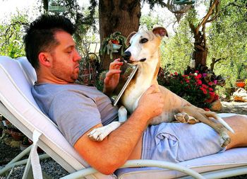 Midsection of man with dog sitting by tree