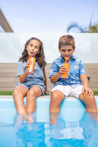 Two kids drinking orange juice in the swimming pool