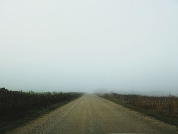 Road amidst field against sky during foggy weather