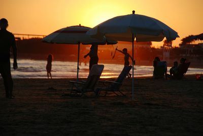 Silhouette people on beach against sky during sunset