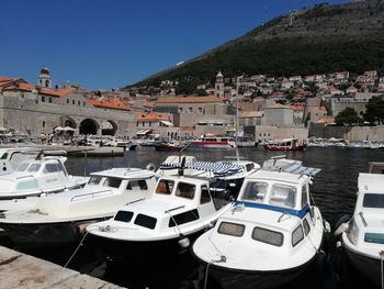 Boats moored at harbor by buildings against sky