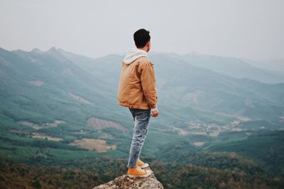 Rear view of man standing on cliff against sky