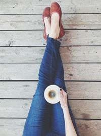 Low section of woman holding coffee cup while sitting on wooden floor