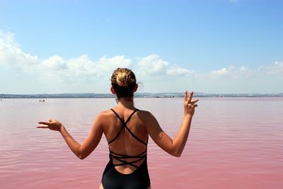 Rear view of woman gesturing peace sign by sea against sky