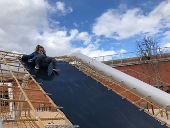 Low angle view of girl sliding down outdoor play equipment