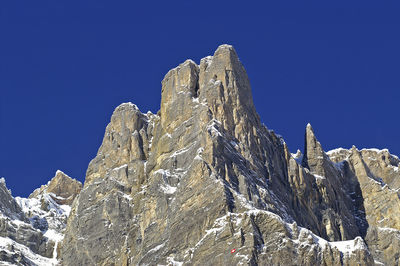 Low angle view of rocky mountain against clear blue sky