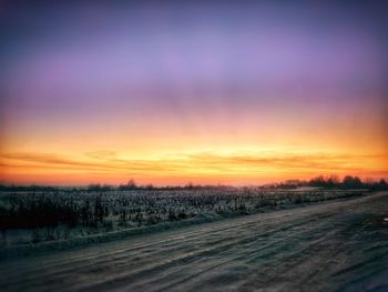 Snow covered road against sky during sunset