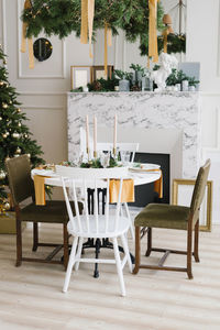 Stylish festive christmas table with vintage chairs near the marble fireplace and christmas tree 