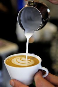 Cropped hand pouring milk in coffee at cafe