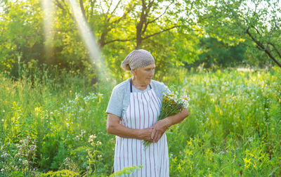 Senior woman holding bunch of flowers in field