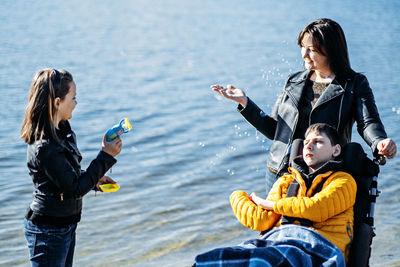 Happy family, mother, daughter and son with cerebral palsy spending time together on the river bank