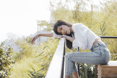 Portrait of woman sitting on railing against plants