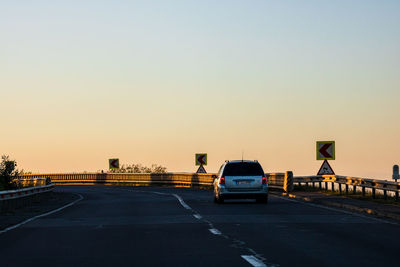 Cars on road against clear sky during sunset