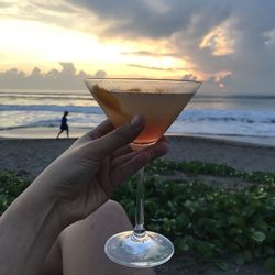 Midsection of person holding ice cream at beach against sky during sunset