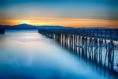 Wooden posts in sea against sky at sunset