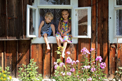 Happy 5-6 years old girl and her little brother sitting on the window sill in the house in village