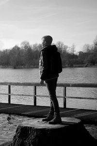 Rear view of man standing on pier over lake against sky