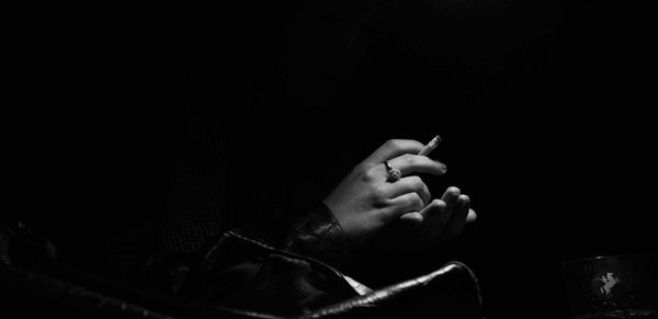 Cropped hands of woman holding cigarette against black background