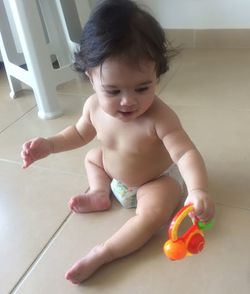 High angle view of shirtless cute baby girl playing with toy on floor at home