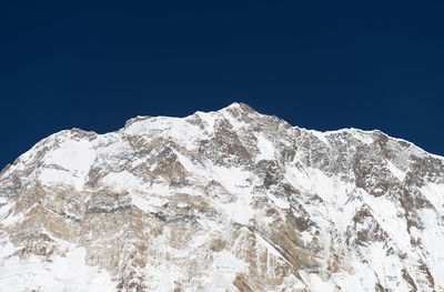Low angle view of snowcapped mountain against clear blue sky