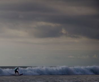 Man surfing in sea against cloudy sky at dusk