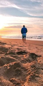 Rear view of man on beach against sky during sunset