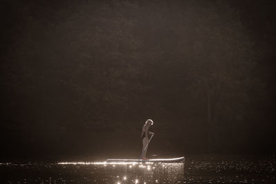 Woman paddleboarding on lake against trees in forest