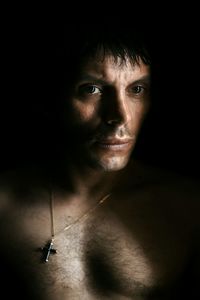 Close-up of shirtless man looking away against black background