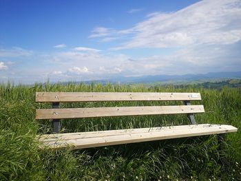 Empty bench on field against sky