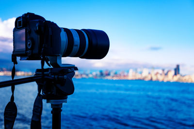 Close-up of camera against sea and cityscape against sky